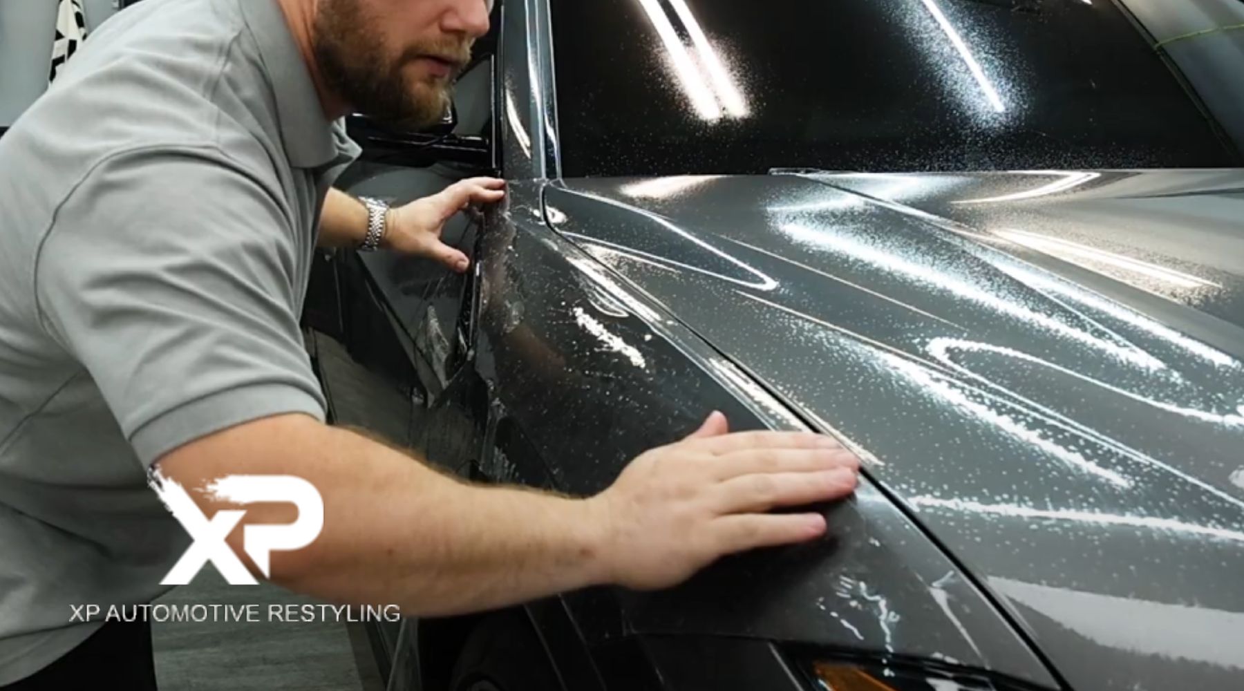 A technician applies a paint protection film to the hood of a car, ensuring a smooth finish. The image features the logo of "XP Automotive Restyling," highlighting their expertise in automotive restyling services.