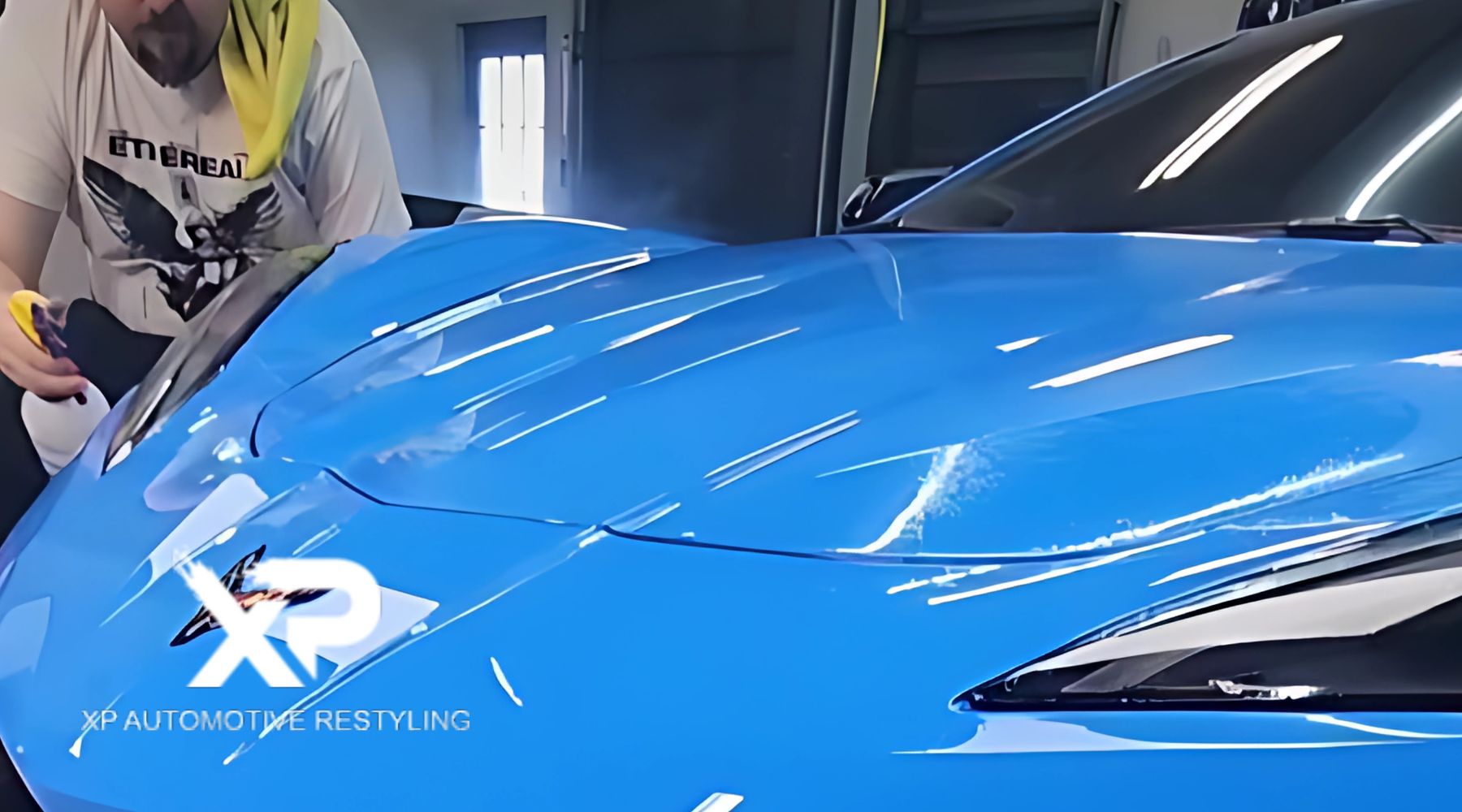 A person detailing the hood of a bright blue car with a microfiber cloth and a detailing tool. The logo "XP Automotive Restyling" is prominently displayed on the lower portion of the image.