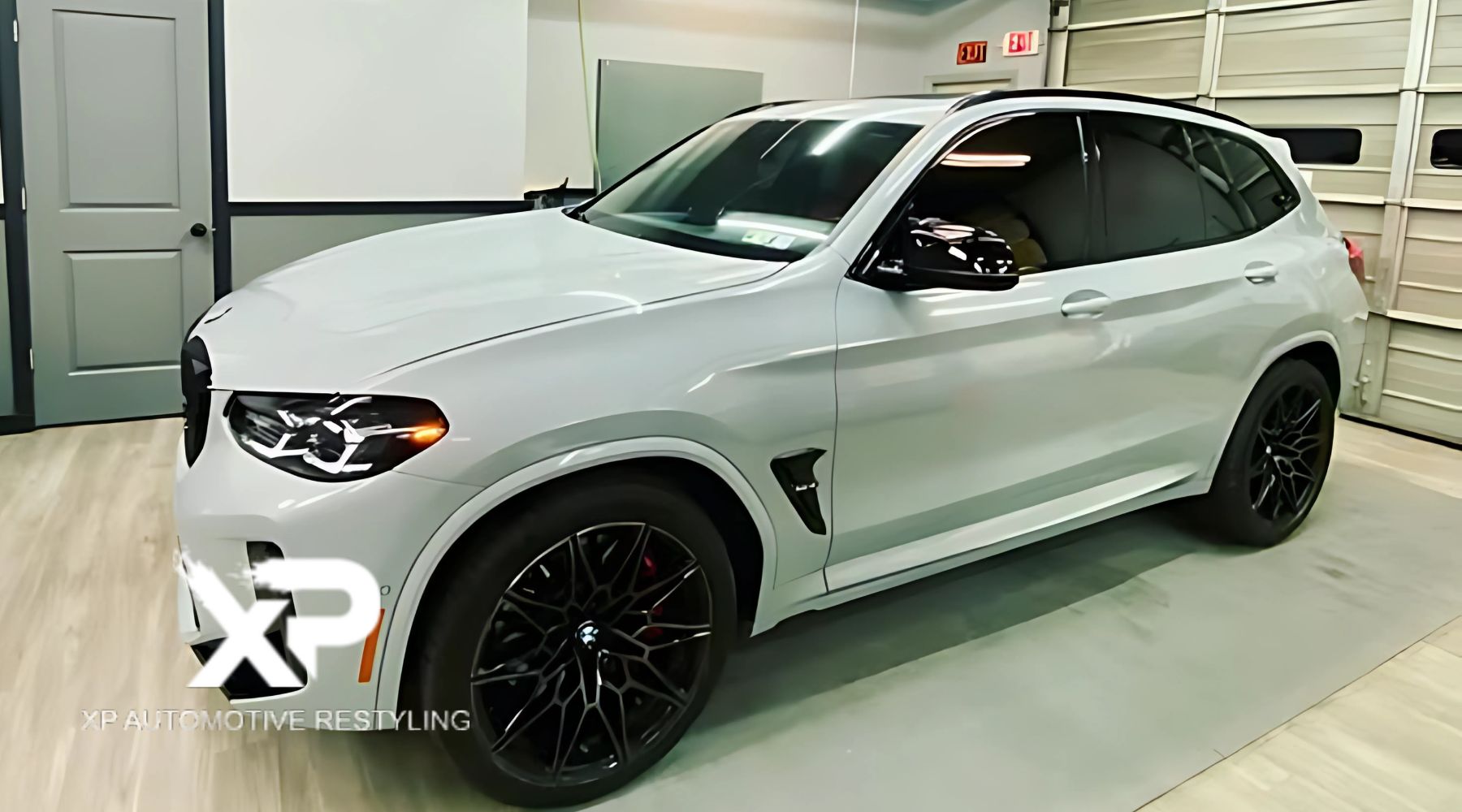 A sleek white luxury SUV with black alloy wheels, showcased in a modern garage setting. The car's polished exterior reflects the lighting, highlighting its clean design and shiny finish.