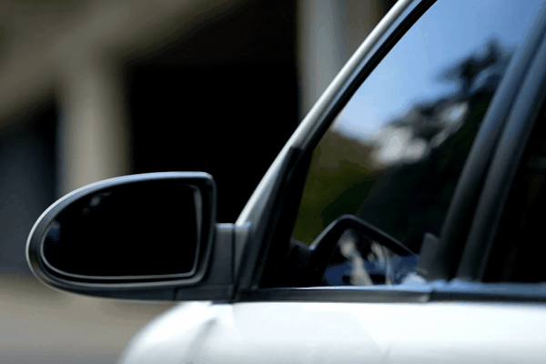 A close-up of a car’s side mirror and tinted window reflecting subtle outdoor surroundings, showcasing a sleek, polished appearance and glare reduction benefits.