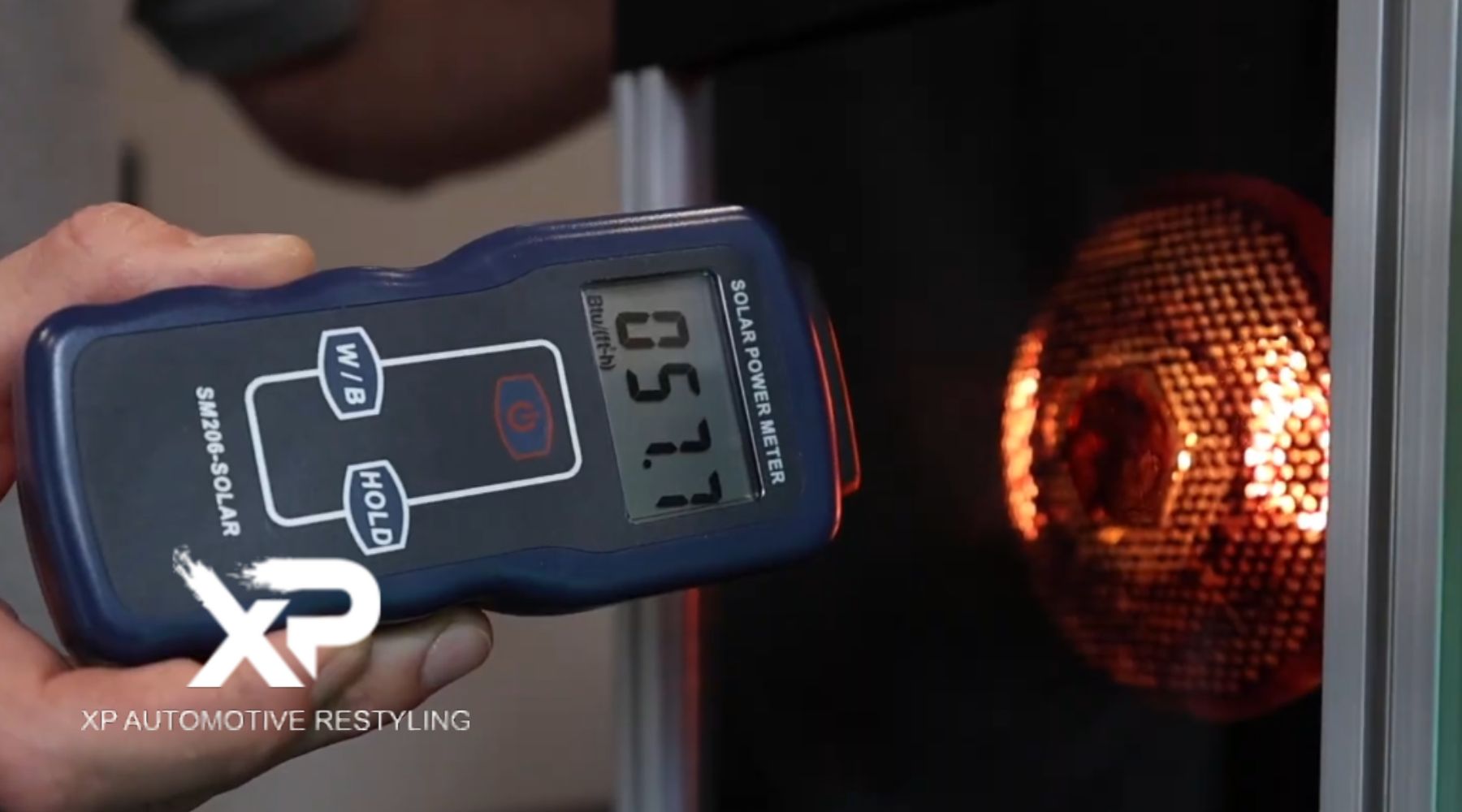 A hand holding a solar power meter displaying "0577" as it measures solar energy from a heat source with a glowing orange honeycomb pattern. The XP Automotive Restyling logo and text are displayed in the bottom corner.