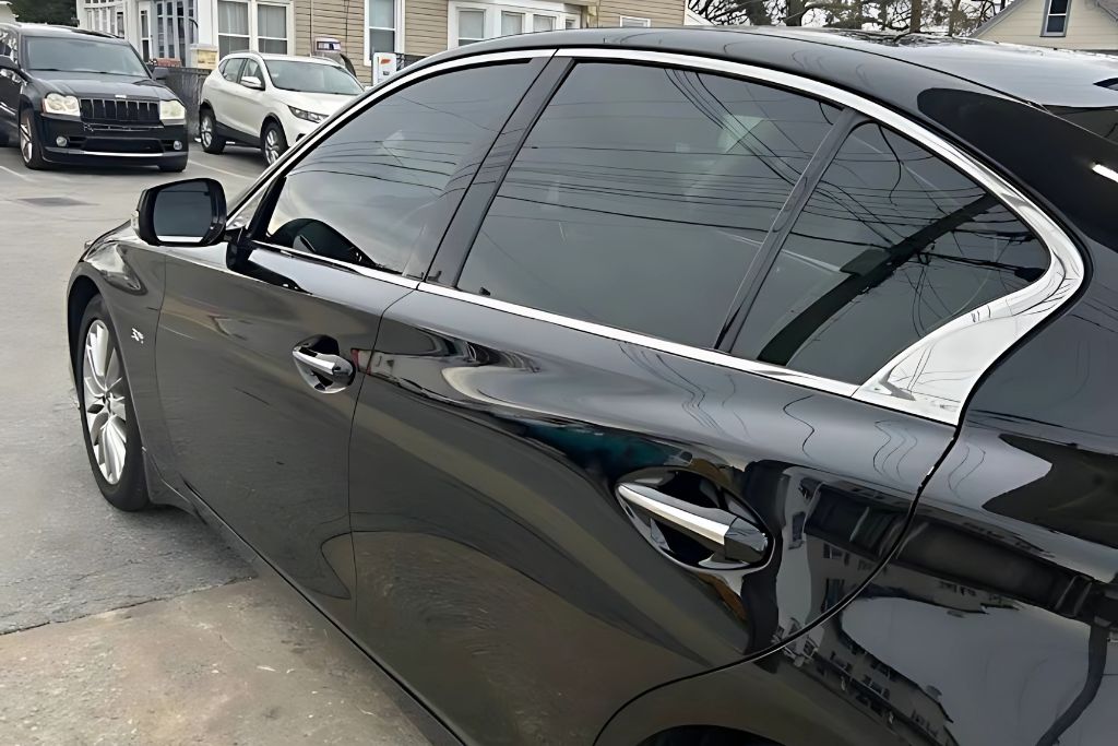 A glossy black sedan with tinted windows and a flawless finish is parked outdoors, showcasing the smooth, reflective surface protected by paint protection film.