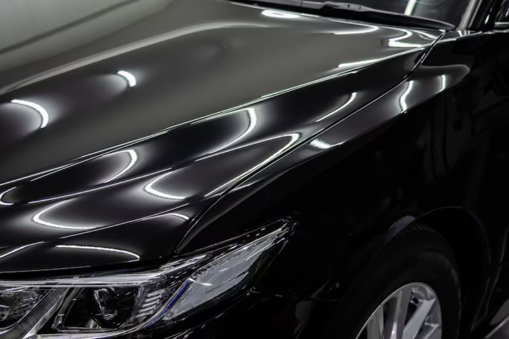 Close-up of a glossy black car hood and headlight, showcasing the deep shine and flawless reflection created by a professional ceramic coating application.