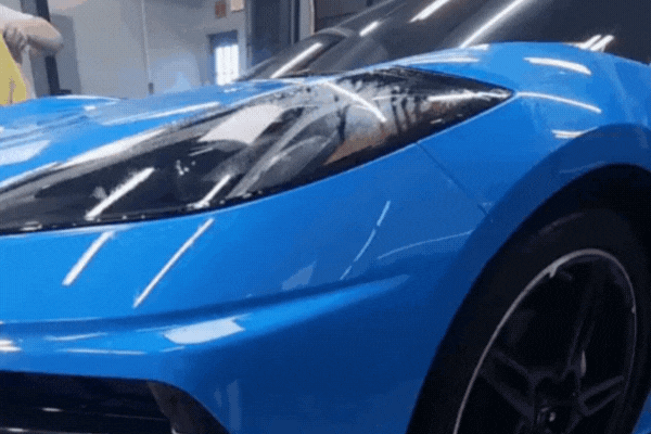Close-up of a vibrant blue sports car's hood and headlight as water beads and rolls off smoothly, demonstrating the hydrophobic effect of a freshly applied ceramic coating.