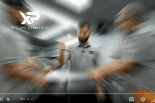 A dynamic, fast-paced clip showing three team members from XP Automotive Restyling stretching and puncture-testing a piece of clear paint protection film. They wear matching branded shirts, highlighting teamwork and the durability of their product. The XP Automotive Restyling logo is visible in the top left corner.