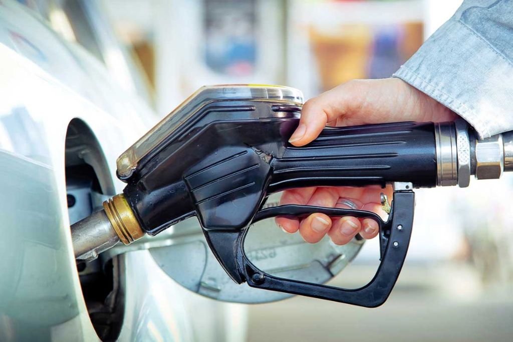 Close-up of a hand refueling a vehicle at a gas pump, symbolizing how window tint can help reduce A/C usage and improve overall fuel efficiency.