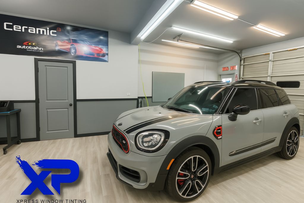 A sleek grey Mini Cooper with dark tinted windows parked inside XP Automotive Restyling's studio, showcasing a clean, high-contrast aesthetic upgrade using ceramic window film.