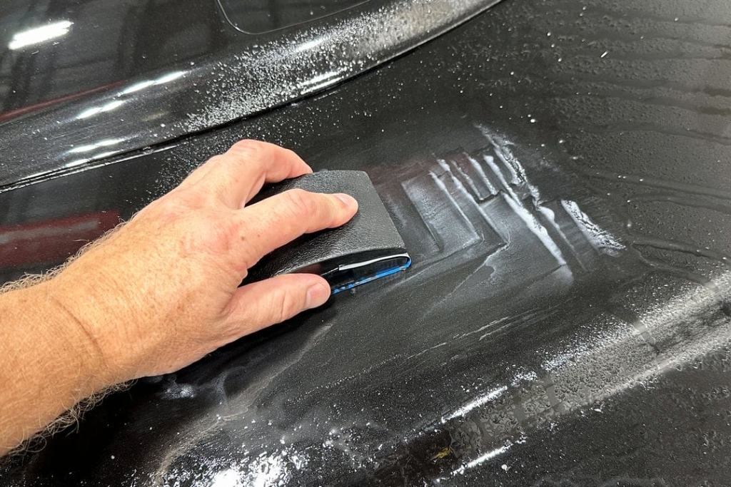 Wet Sanding — close-up of a hand using a sanding block with lubricant on a black car surface in Southampton, PA to remove tough ceramic coating as a last resort