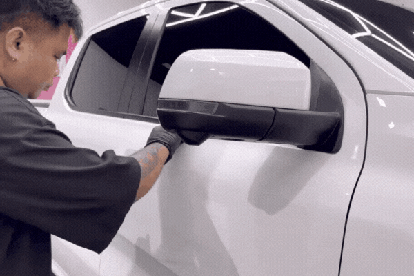 Detailing professional in gloves carefully applying nano-ceramic coating to a white vehicle’s side mirror in a controlled environment, illustrating how nano-ceramic coating bonds to the surface to protect against damage while enhancing gloss.