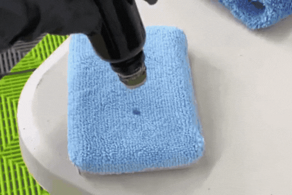 A gloved hand applies a drop of ceramic coating onto a blue microfiber applicator pad, prepping it for even application to a vehicle’s surface. This visual demonstrates the beginning steps of professional ceramic coating application at XP Automotive Restyling.