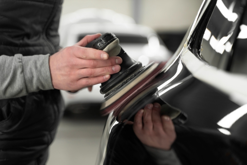 Close-up of a person using a dual-action polisher on a glossy black car panel during paint correction, a crucial prep step in ceramic coating application. Proper surface preparation like this directly impacts how long ceramic coating lasts on a vehicle.