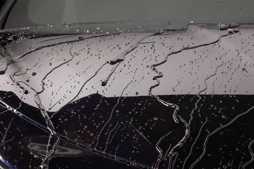Close-up of a car hood with water beading inconsistently on the surface, showing reduced hydrophobic effect—one of the signs your ceramic coating needs reapplication.