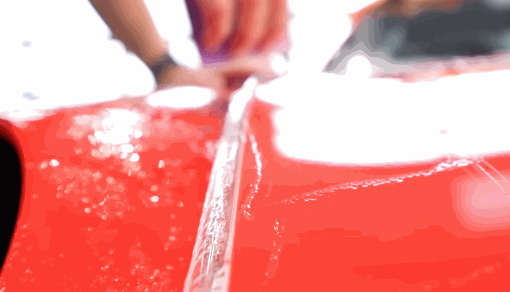 A technician carefully smooths out paint protection film along the panel of a bright red car, ensuring full coverage.