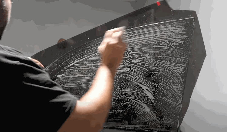 A person scrubs a large car window with soapy water to prepare the surface for window tint installation, ensuring it's free of dust and debris.