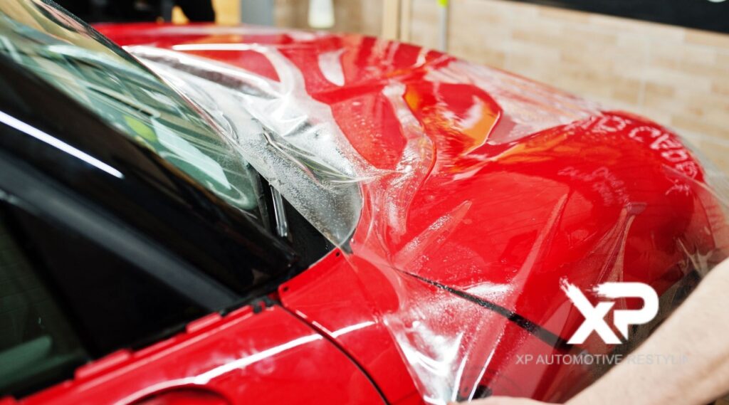 Professional installation of clear paint protection film on a red car hood at XP Automotive Restyling in Southampton, PA.
