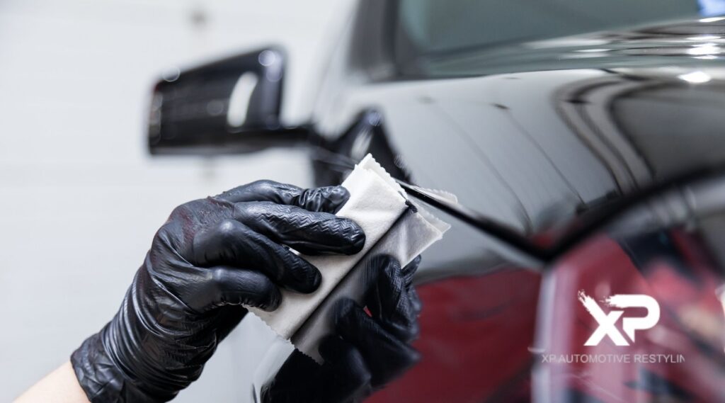 Technician wearing black gloves applying ceramic coating to a car’s glossy paint surface at XP Automotive Restyling.