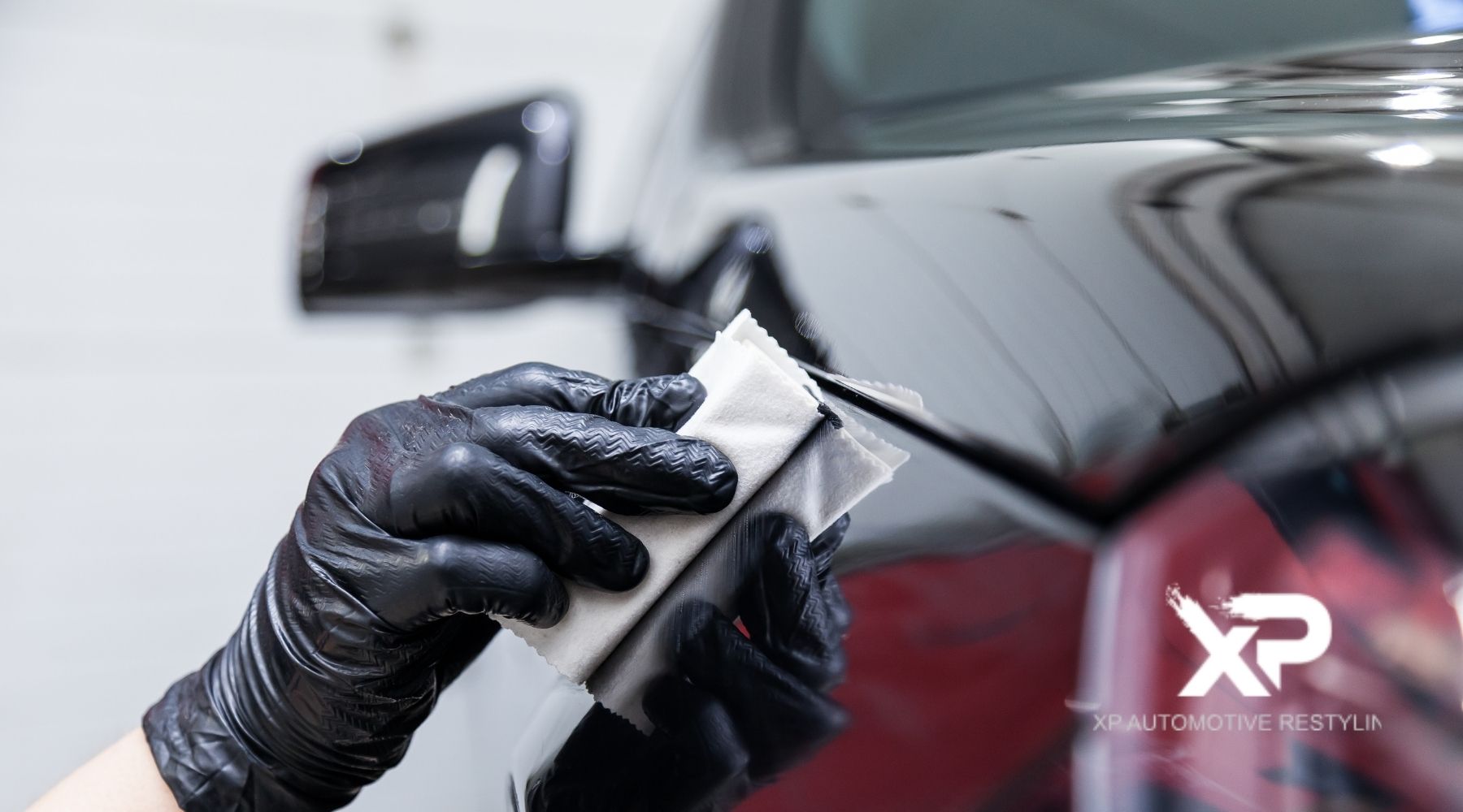 Technician wearing black gloves applying ceramic coating to a car’s glossy paint surface at XP Automotive Restyling.
