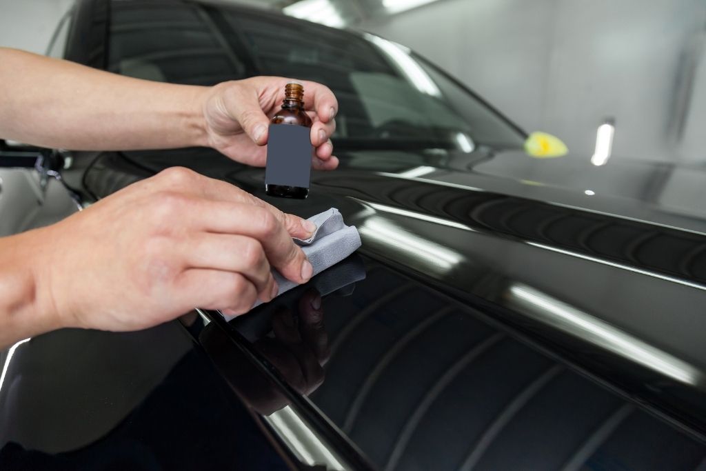 Technician applying nano ceramic coating to a black car hood using an applicator block for long-term paint protection.