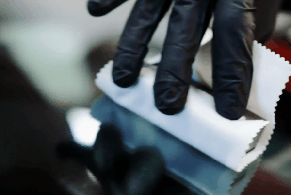 Close-up of a technician applying ceramic coating to a vehicle’s paint using a microfiber applicator and protective gloves.
