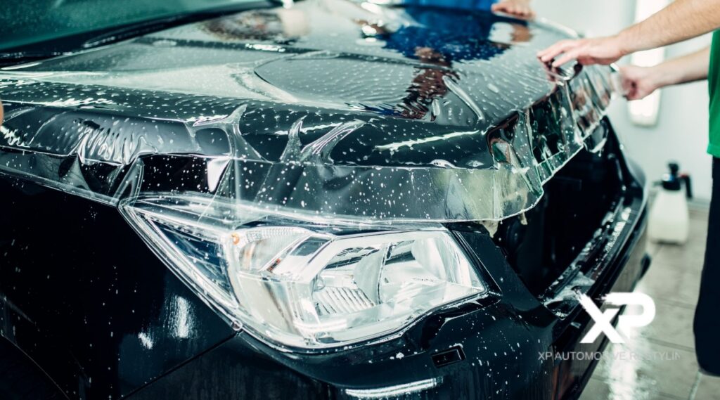 Technician installing paint protection film on the hood of a black car during the PPF installation process.