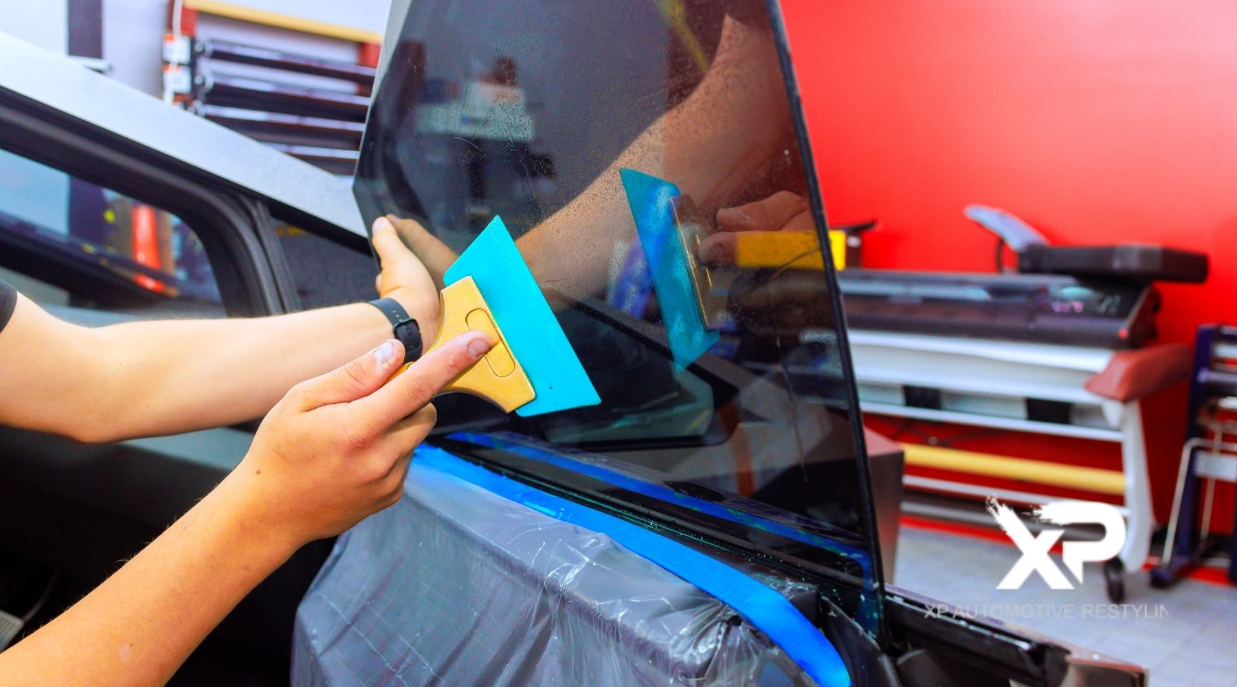 Technician applying window tint film to a car door window using a squeegee at XP Automotive Restyling.