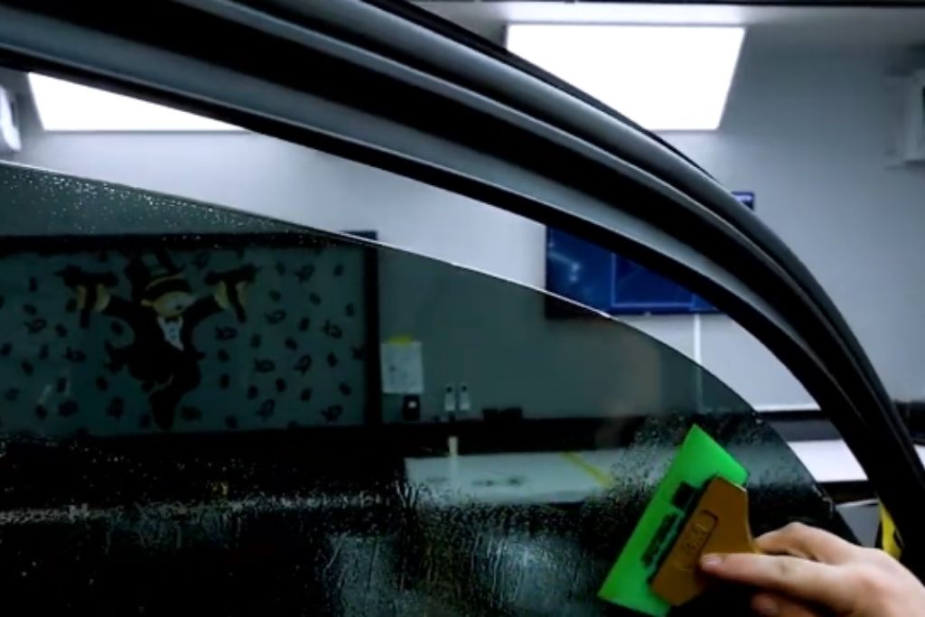 Close-up of a technician applying window tint film to a car door glass using a squeegee during installation.