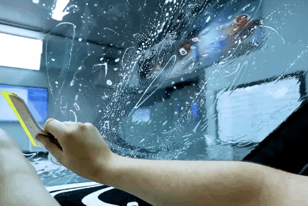 Close-up of a technician smoothing wet window tint film onto a car window during installation.