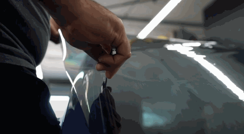 Technician carefully trims window tint film along the edge of a car window to ensure a precise and seamless window tint finish.