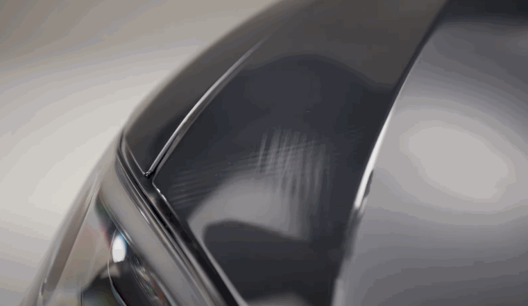 A glossy dark vehicle panel shows a smooth finished layer of paint protection film. Reflections on the surface highlight the clean protected finish.