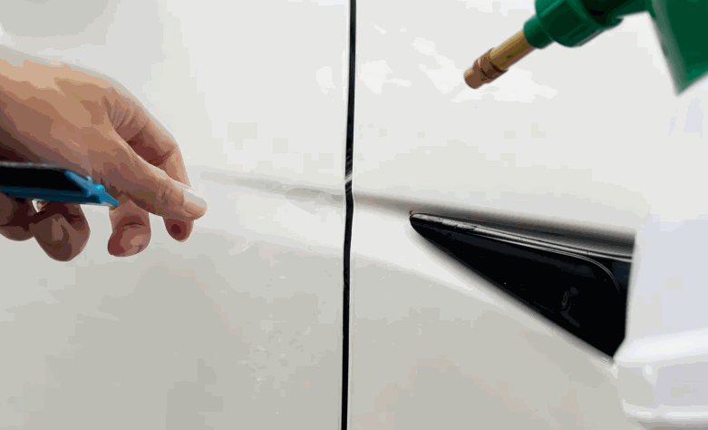 Close-up of paint protection film being fitted along a white car door edge for precise surface protection.