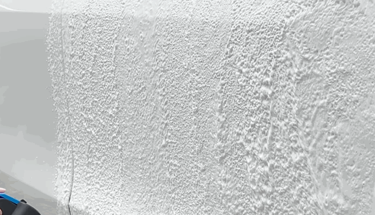 A close up shows a white vehicle panel covered with installation solution before paint protection film is applied. The wet surface is prepared for smooth film placement.