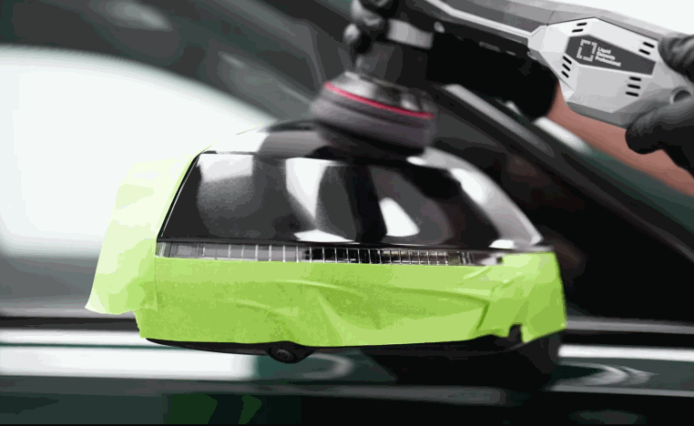 A technician polishes a taped off side mirror on a dark vehicle before ceramic coating is applied.