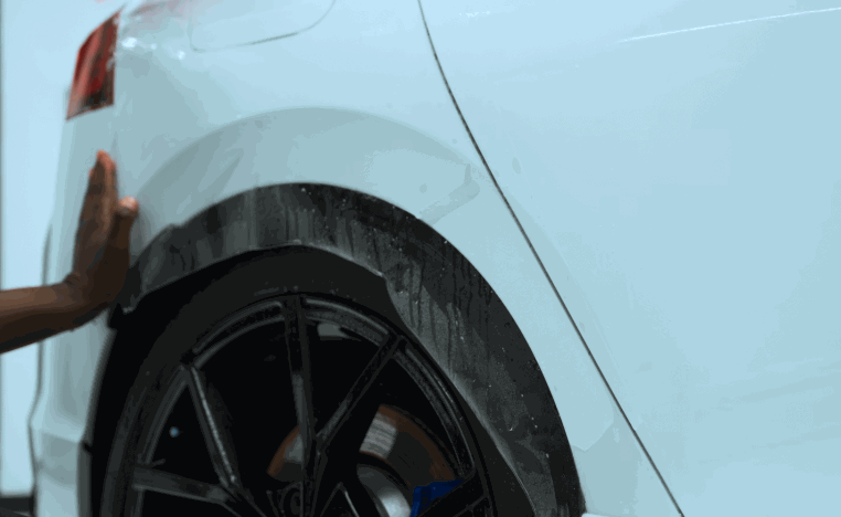 Paint protection film being smoothed around the rear wheel arch of a white vehicle with black wheels.