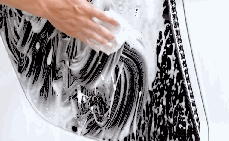 Hand scrubs a white car wheel with thick soap during prep before ceramic coating.