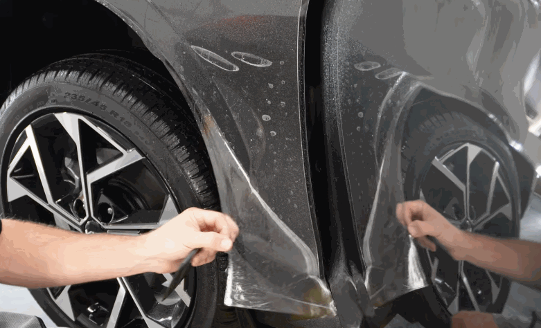 Installer pulls paint protection film around the lower fender near the wheel of a gray car.
