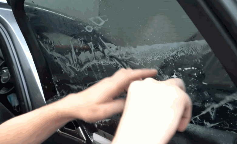 Installer sprays solution across a car window while preparing the glass for window tint application.