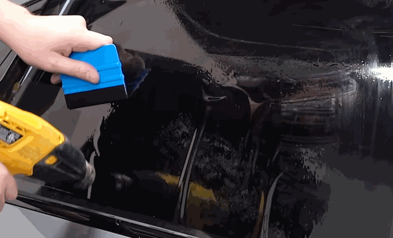 Installer sprays solution across a car window while preparing the glass for window tint application.