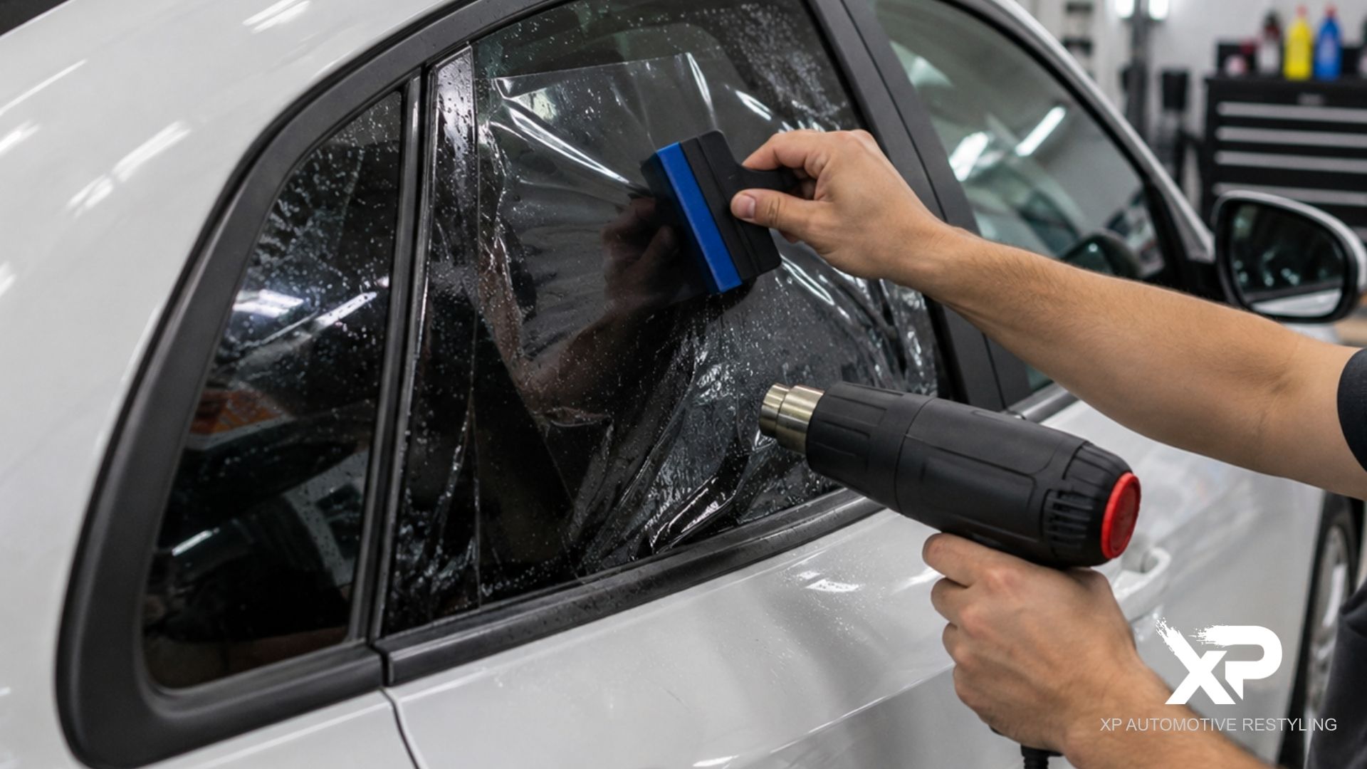 Installer uses a squeegee and heat gun to shape window tint on the rear side window of a white car.
