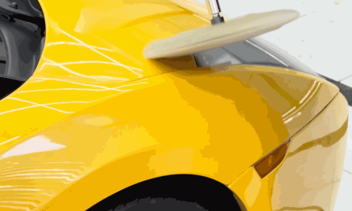 Machine polisher moves across the rear quarter panel of a bright yellow car to refine the paint surface before ceramic coating.
